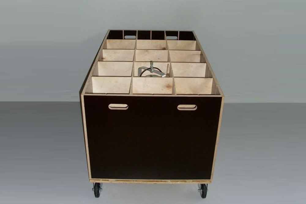 Auf einem Tisch steht eine Holzkiste mit Unterteilungen und Rädern.