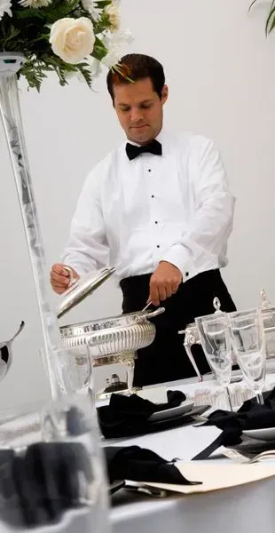 Un hombre con esmoquin está sirviendo comida en una mesa.