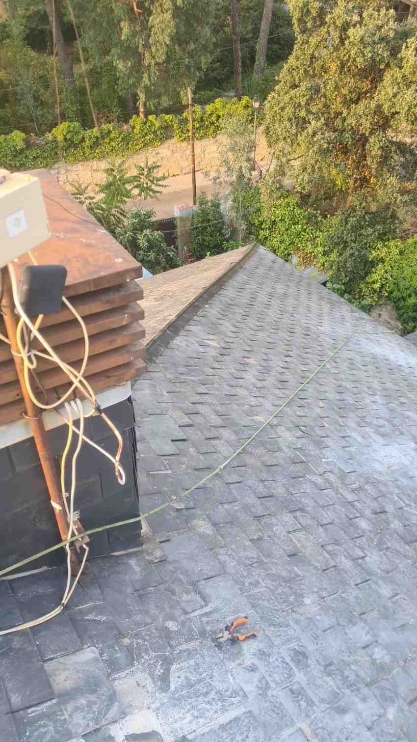 Una persona que lleva un guante de trabajo verde saca un puñado de hojas mojadas y escombros de una canaleta residencial.