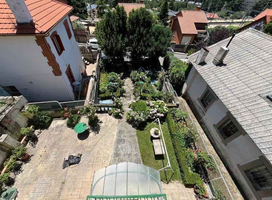 Vista desde un ángulo elevado de un patio ajardinado entre dos edificios con tejados rojos y grises.