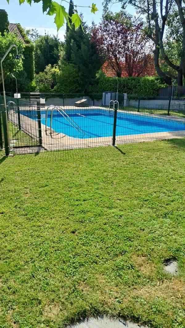 Una piscina rectangular de agua azul brillante se encuentra en un césped verde, rodeada por una valla.