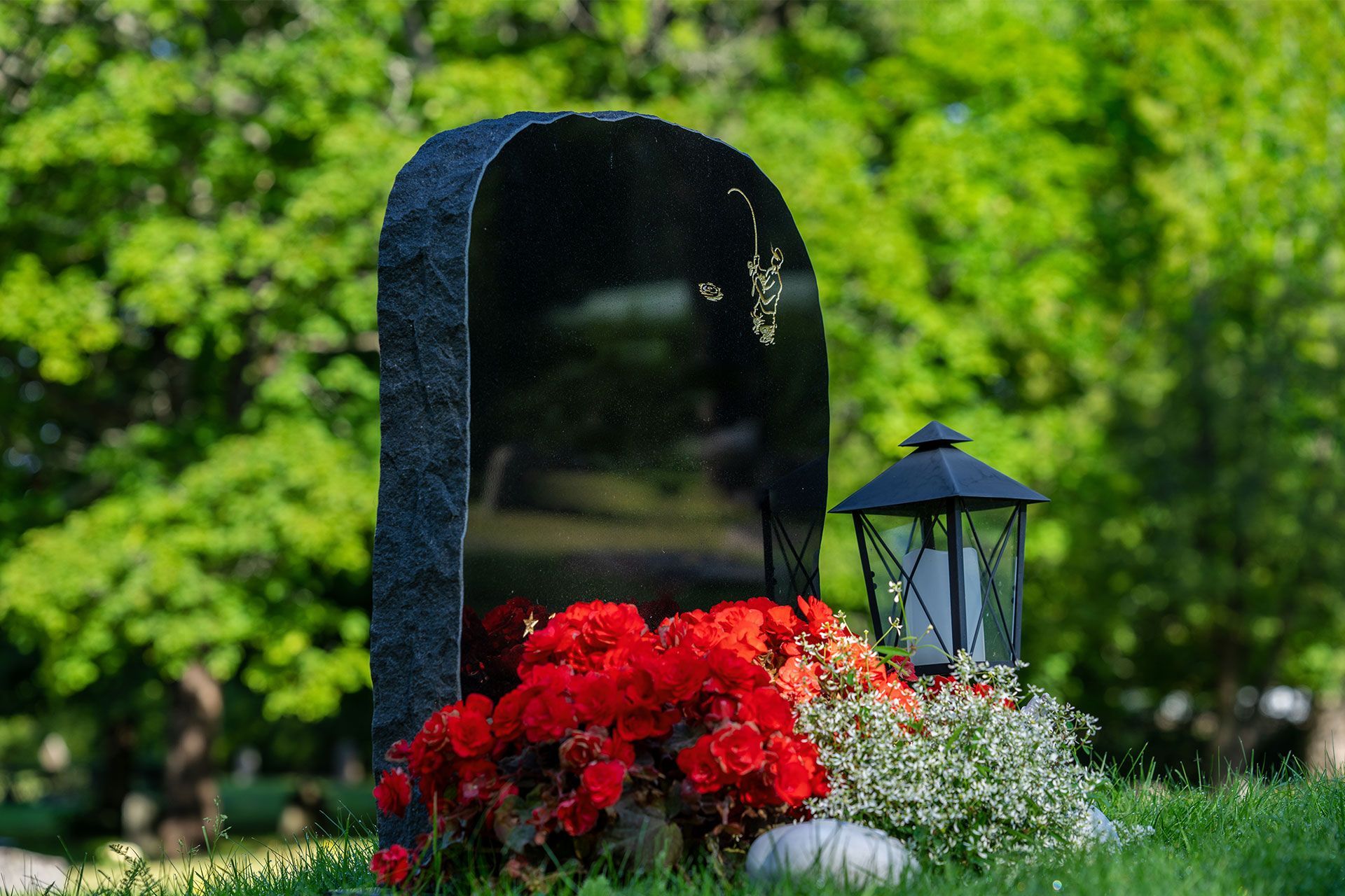 Ein Grabstein mit roten Blumen und einer Laterne auf einem Friedhof.