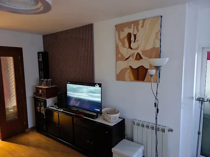 Sala de estar con televisor sobre un mueble negro, lámpara de pie, arte abstracto en la pared y radiador