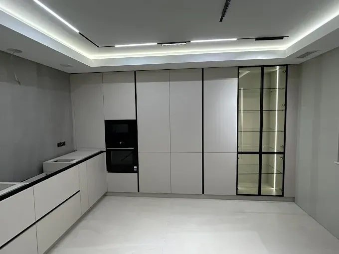 Cocina moderna minimalista con gabinetes blancos, paredes grises y electrodomésticos empotrados negros.