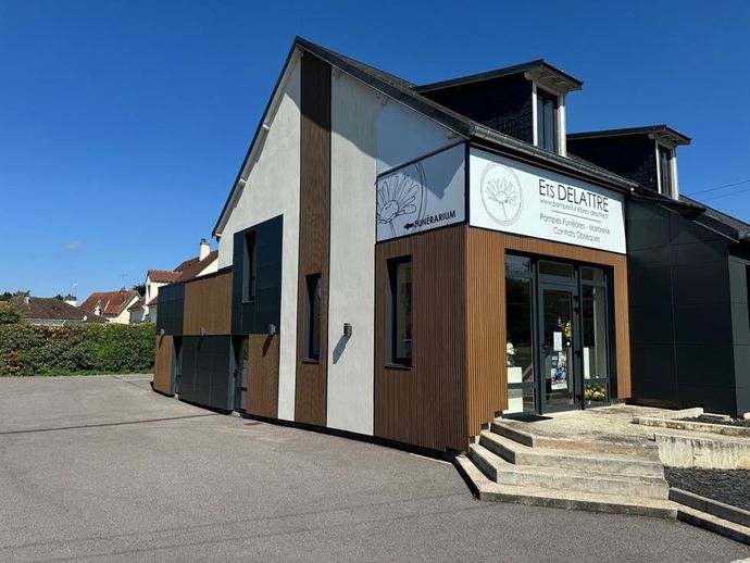 Extérieur d'un bâtiment moderne avec un revêtement brun et blanc, une enseigne indiquant « Encadrine » et un ciel bleu.