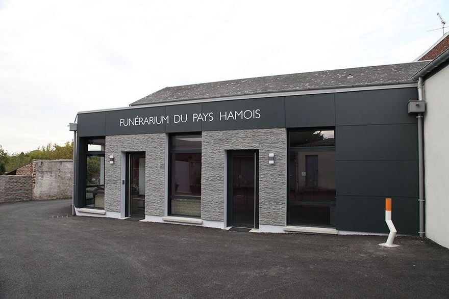 Extérieur d'un bâtiment moderne portant l'enseigne Funérarium du Pays Hamois. Façade grise et noire, plusieurs entrées.