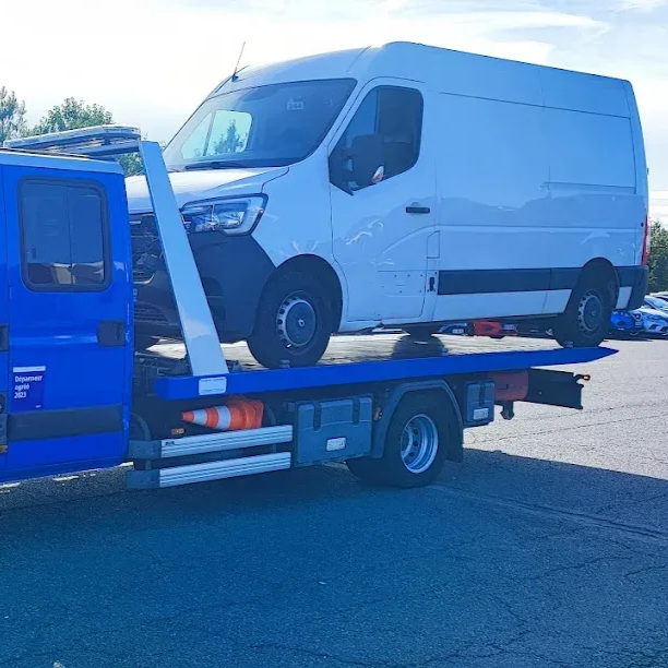 Fourgonnette blanche chargée sur une plate-forme de dépanneuse bleue dans un parking.