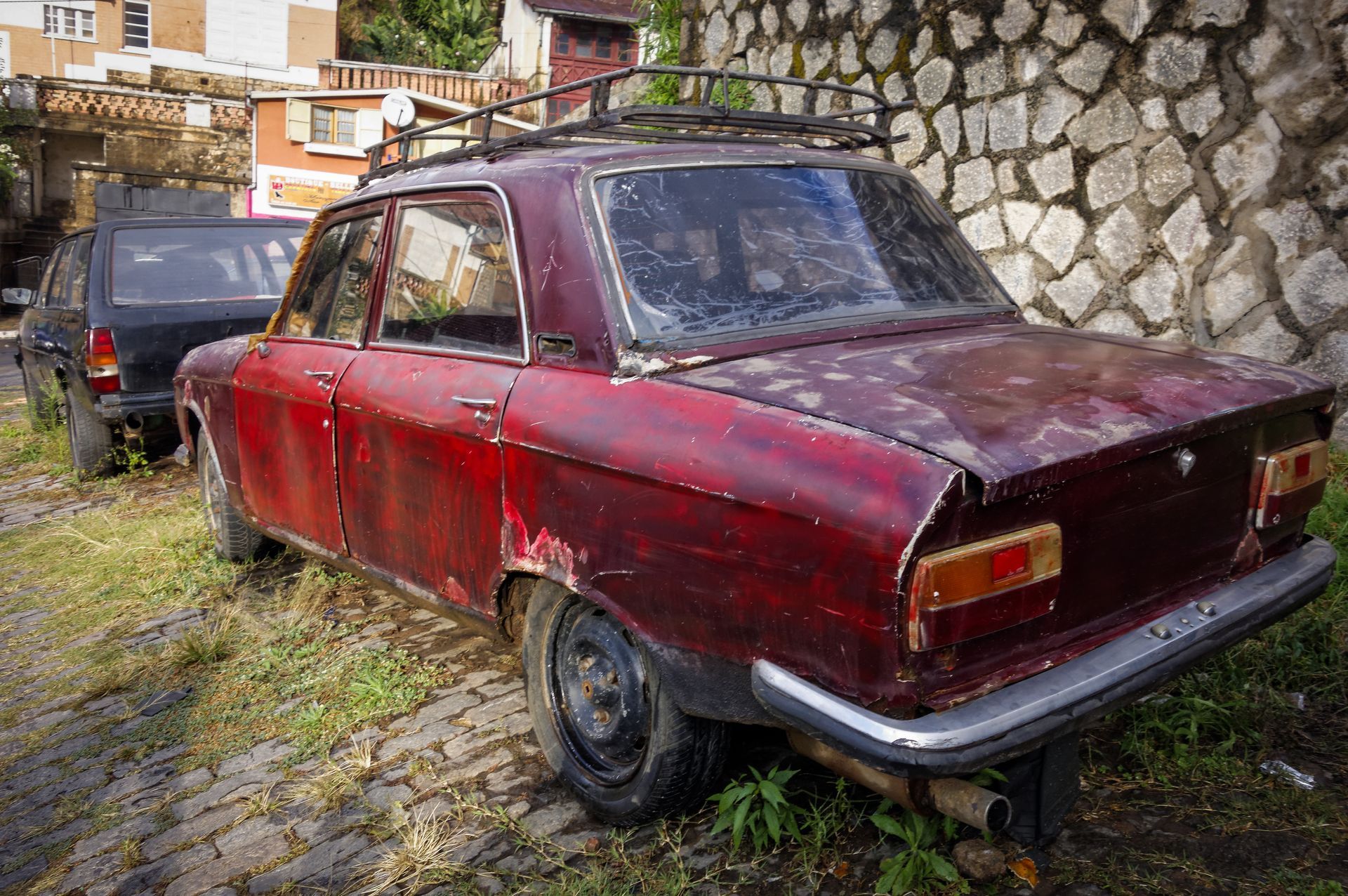 Vieille voiture rouge rouillée garée à côté d'un mur de pierre.