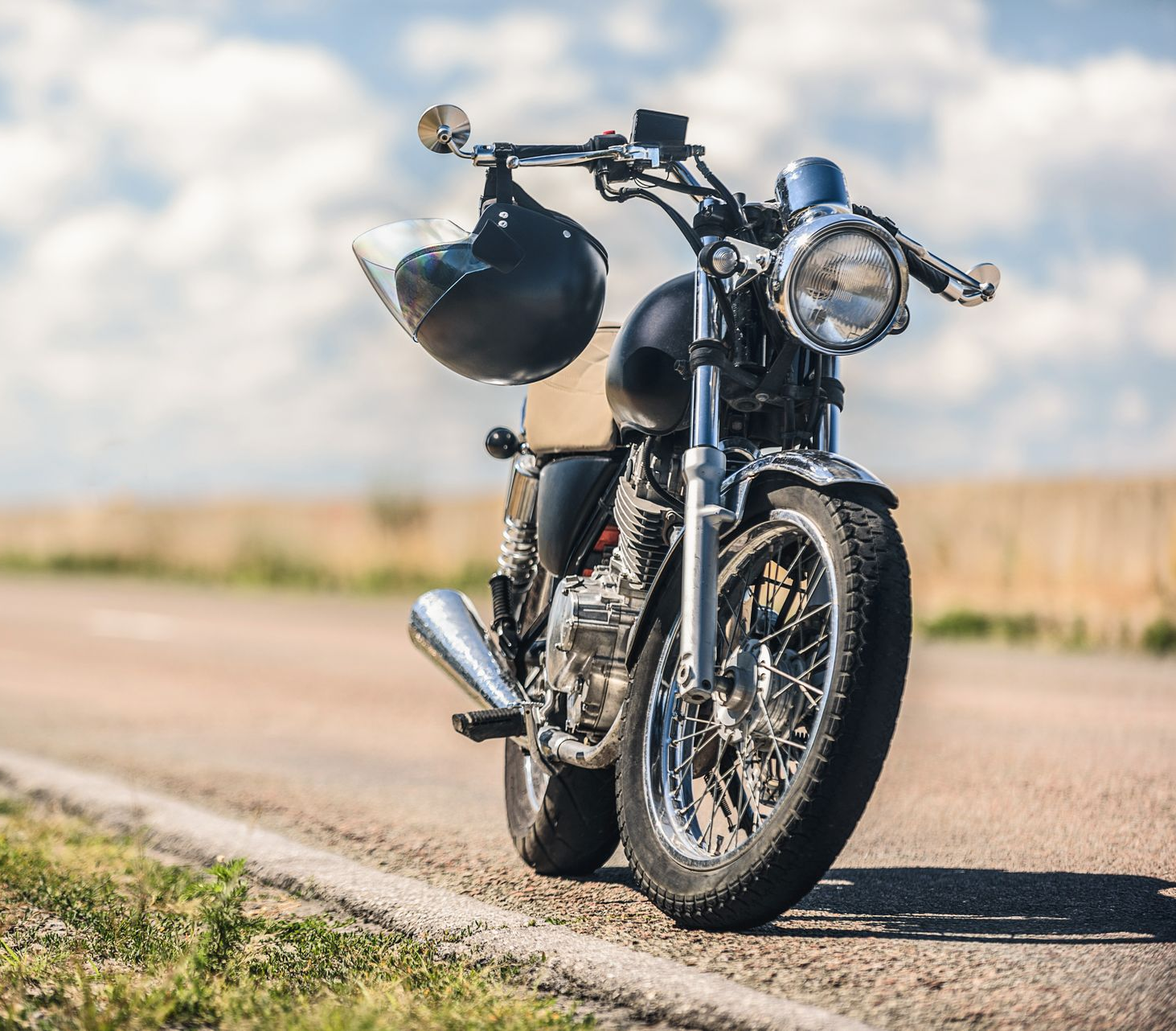 Moto noire avec casque accroché au guidon, garée sur le bord d'une route.