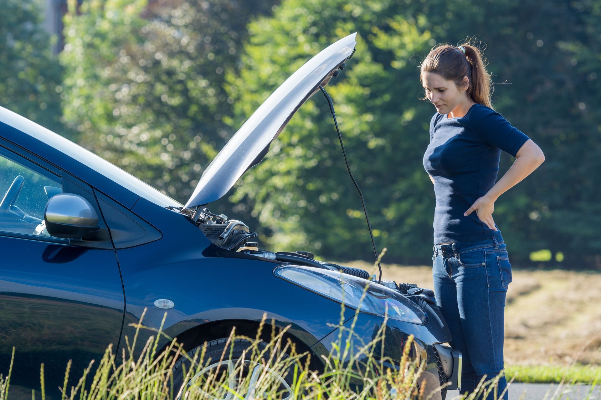 Femme regardant le moteur d'une voiture, capot ouvert, sur la route.