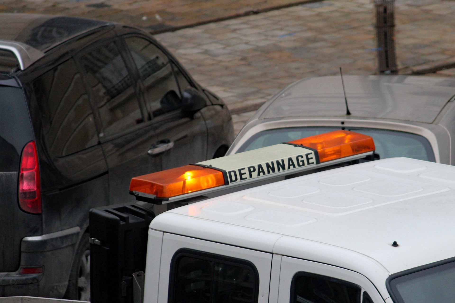 Une dépanneuse avec ses gyrophares orange est stationnée derrière deux véhicules. Le panneau sur le toit indique « DÉPANNAGE ».