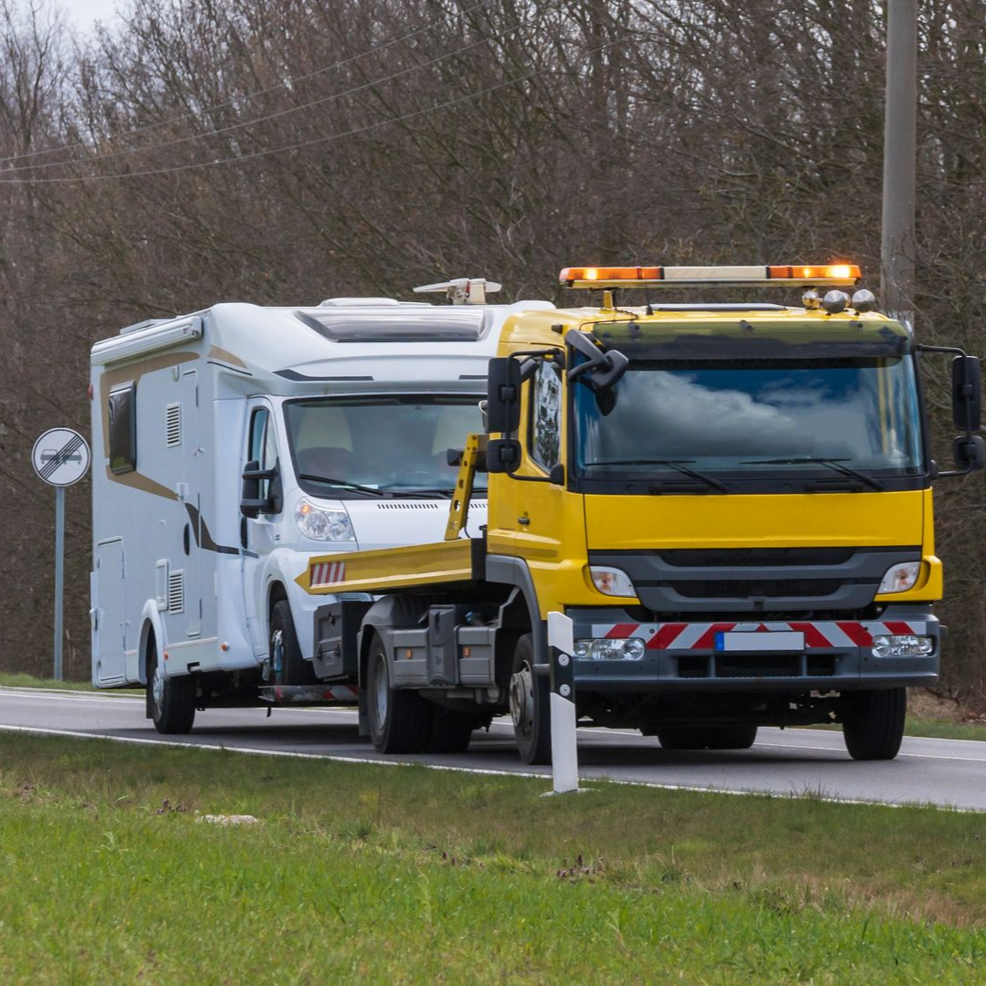 Dépanneuse jaune tractant un camping-car blanc sur une route.