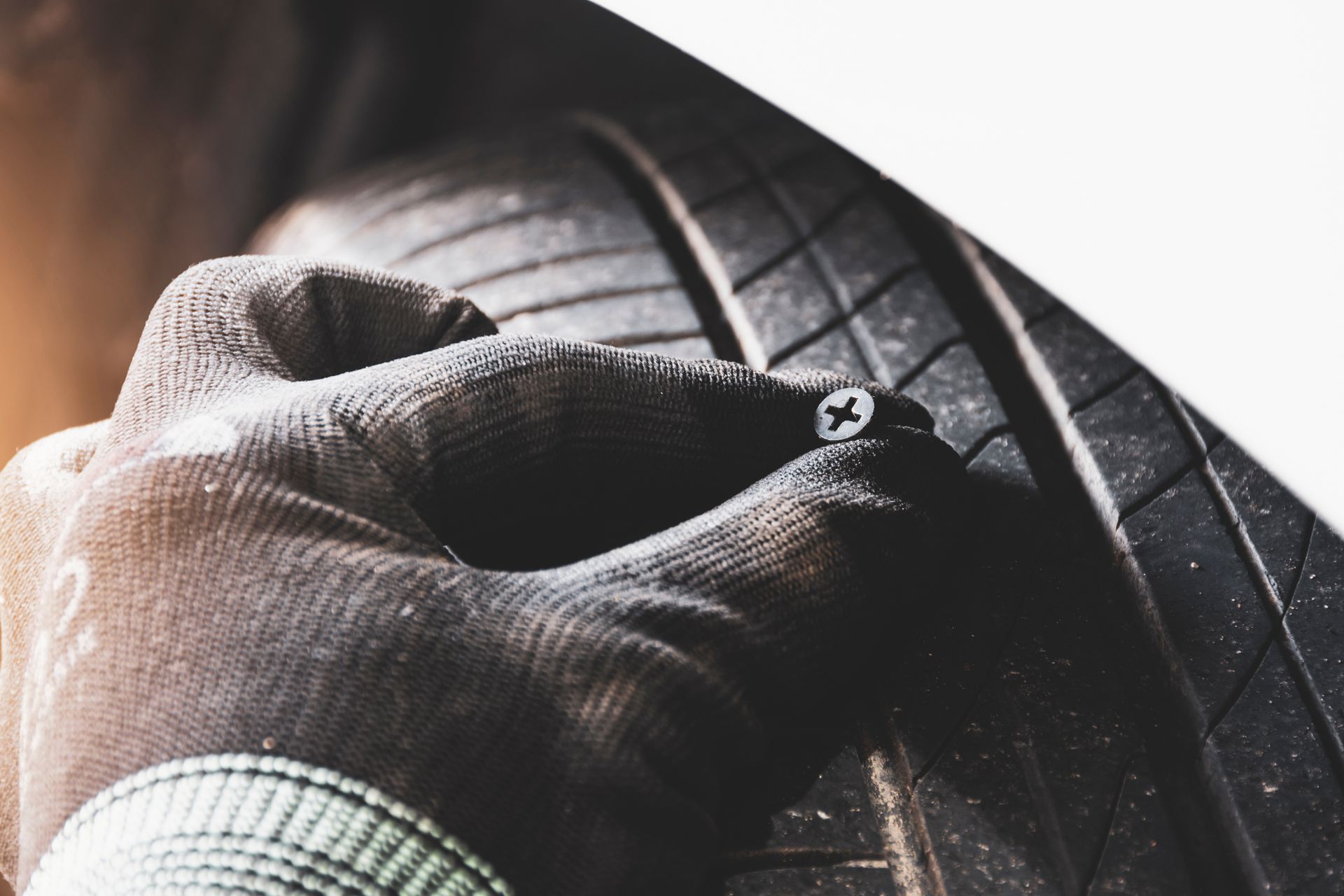 Une main tenant une vis près d'un pneu, indiquant une crevaison.