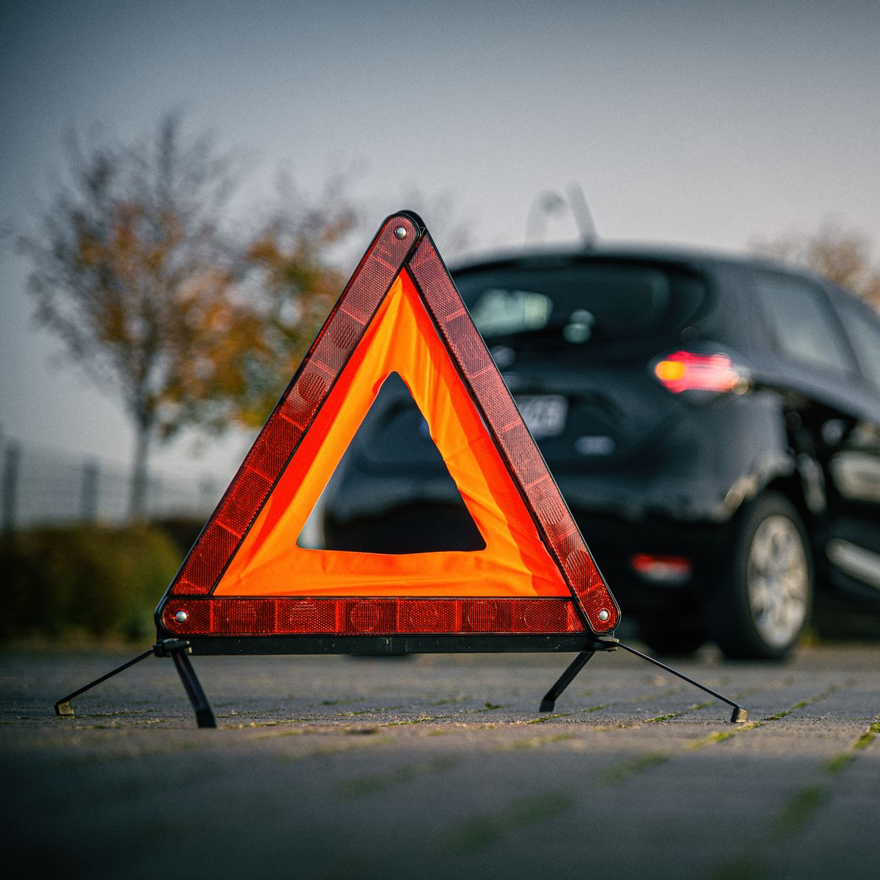 Triangle de signalisation orange et rouge installé sur la route derrière une voiture noire.