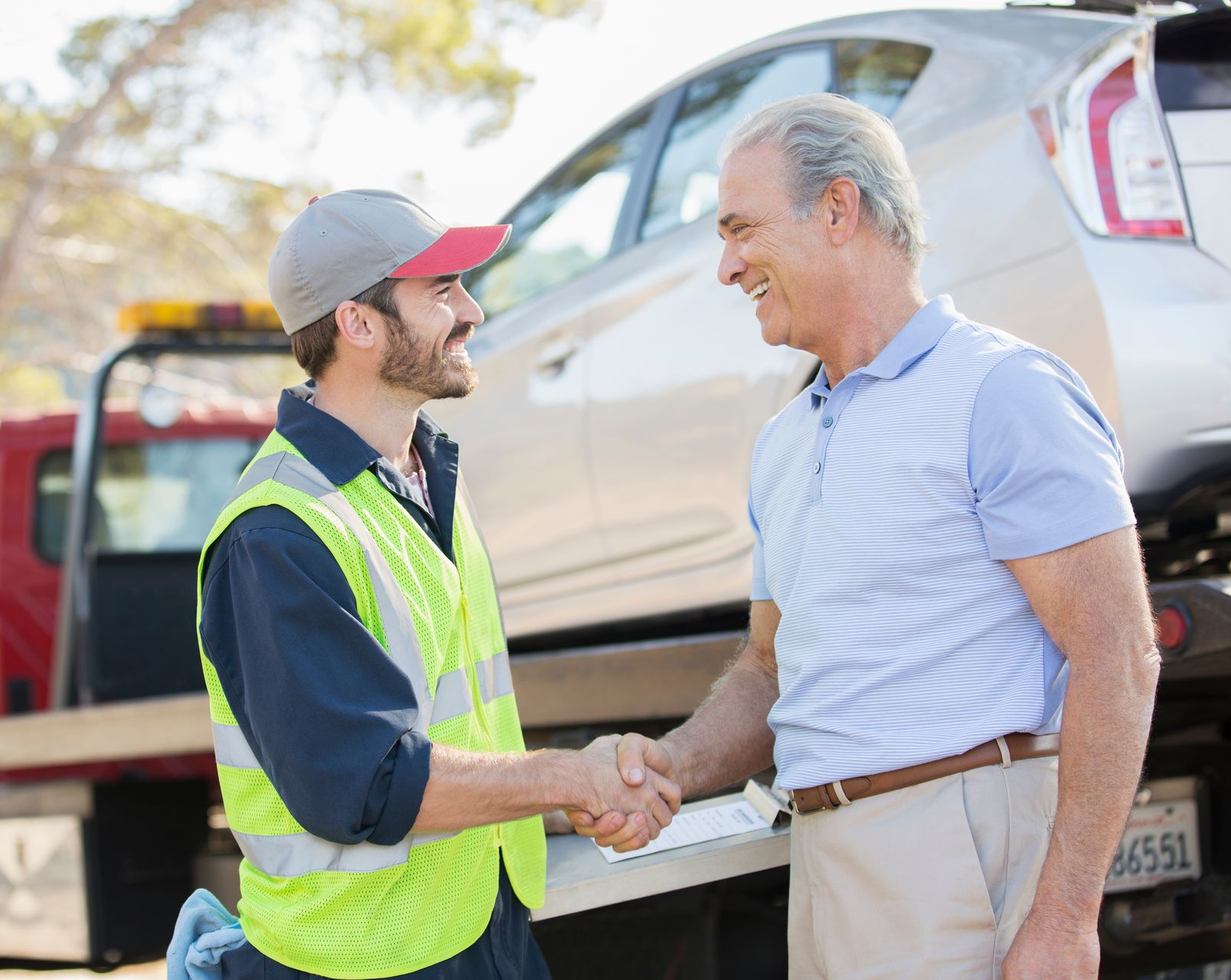 Un dépanneur serre la main d'un homme à côté d'une voiture sur sa dépanneuse.