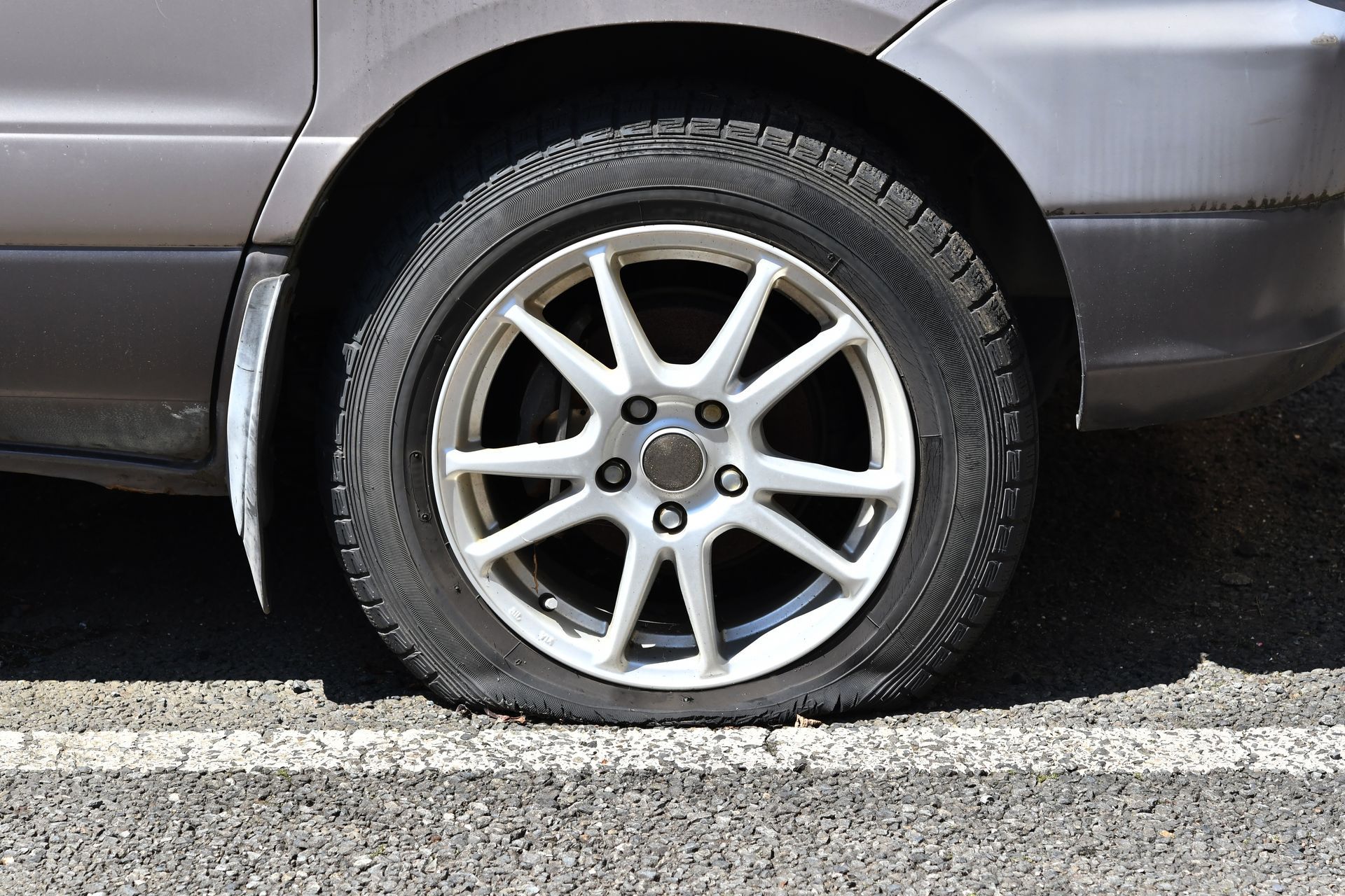 Pneu crevé sur une voiture, la jante est blanche.