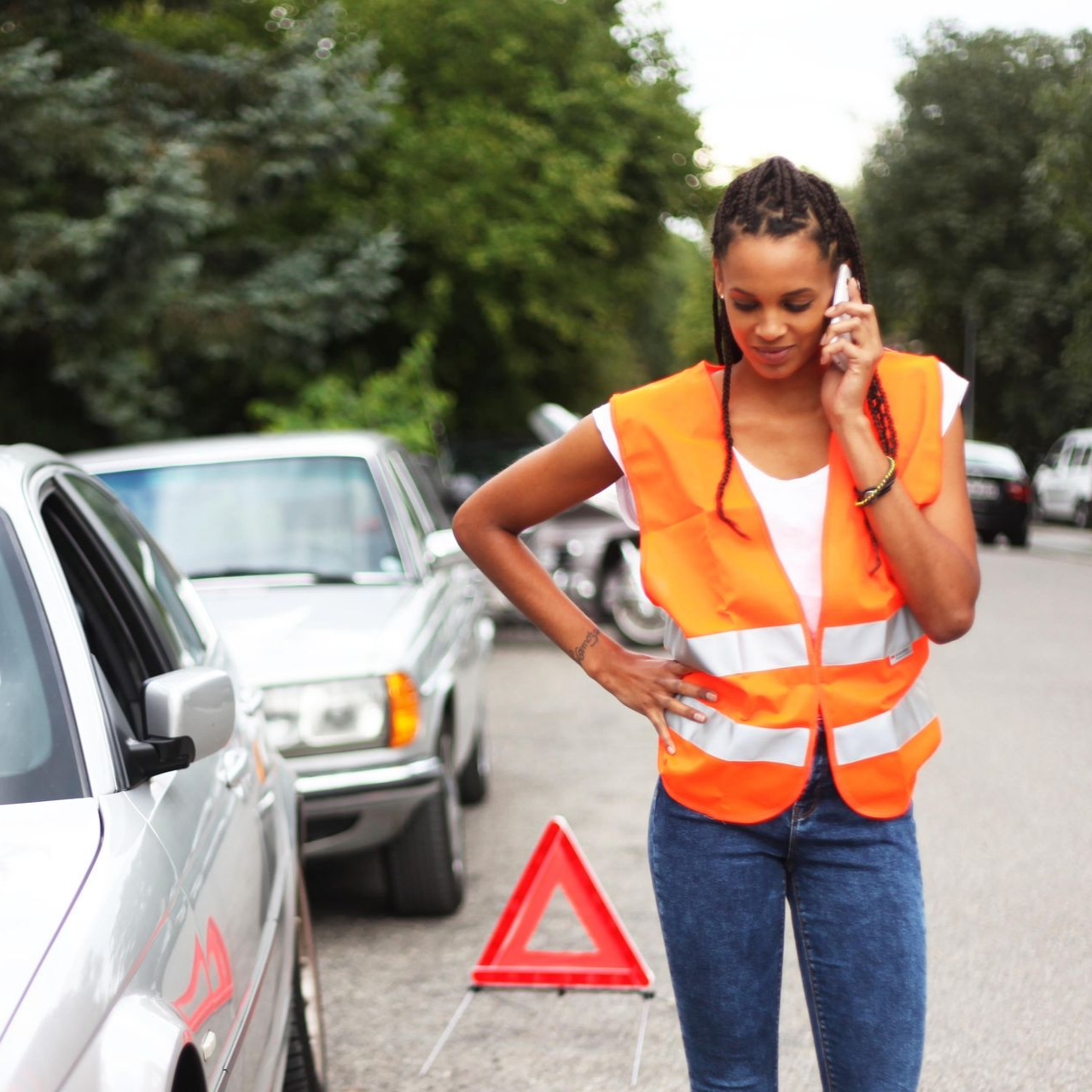 Femme en gilet orange sur le bord de la route parlant au téléphone, accident de voiture, triangle rouge.