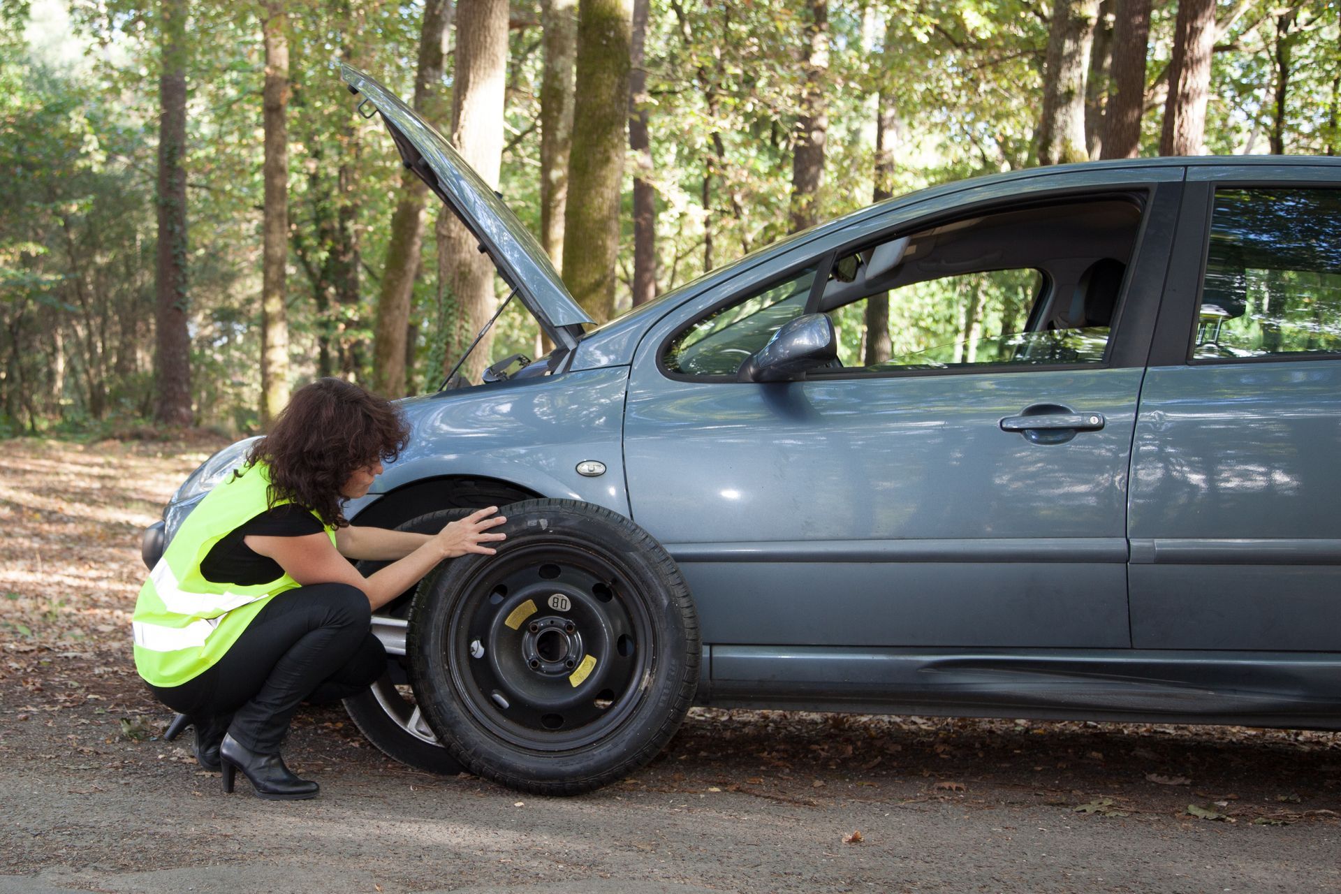 Une femme portant un gilet réfléchissant change un pneu crevé sur une voiture.