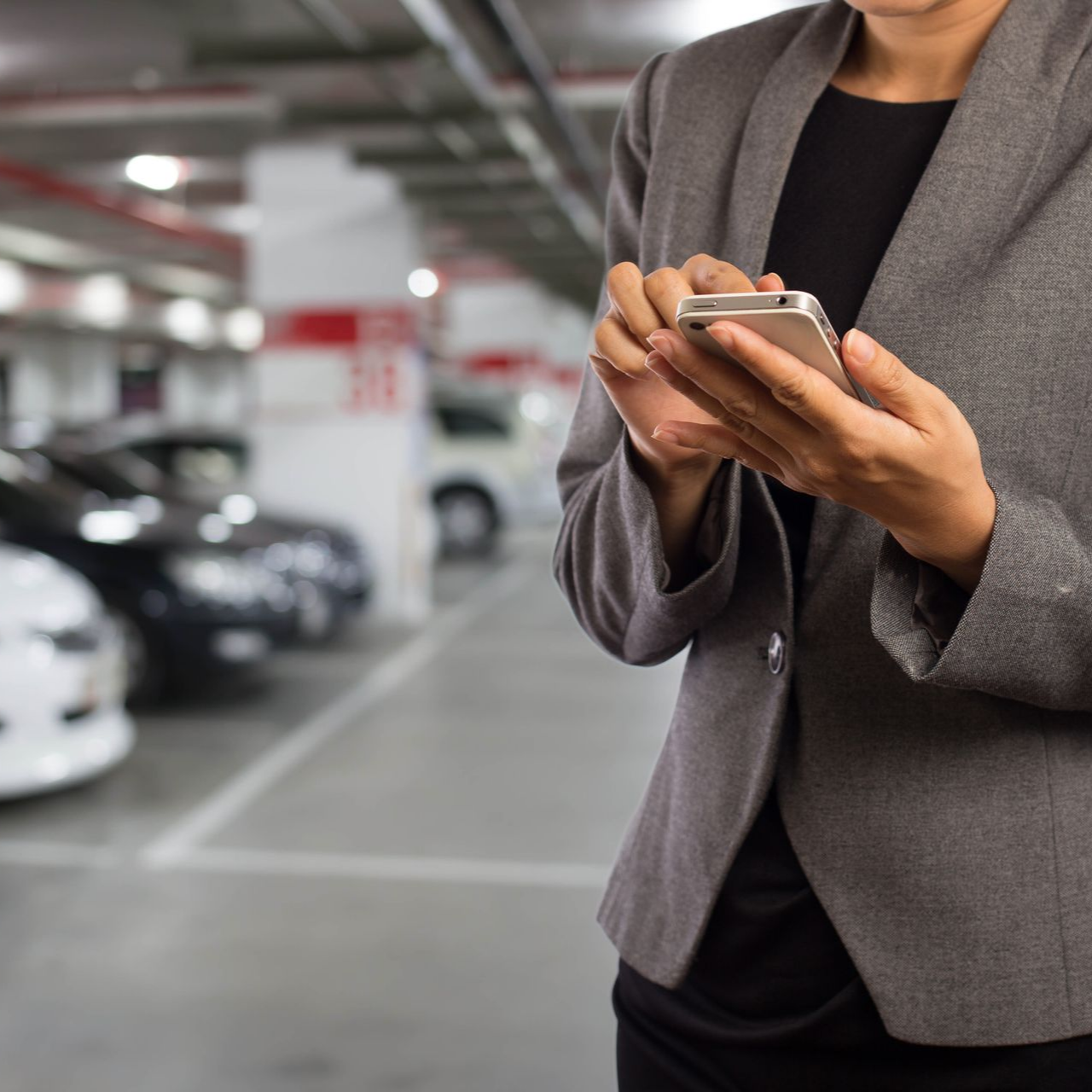 Jeune femme en train de composer un message sur son téléphone dans un parking souterrain