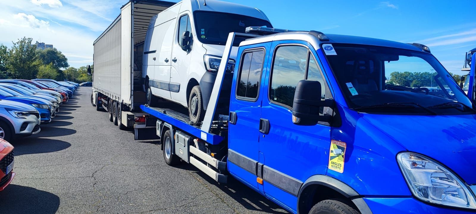 Une camionnette blanche remorquée par une dépanneuse bleue.