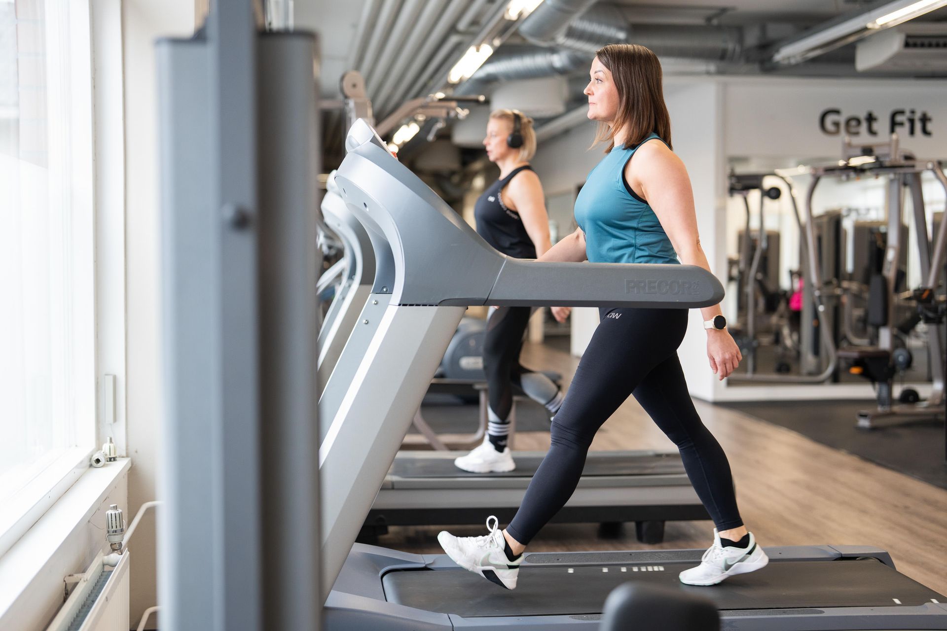 Kaksi naista kävelee juoksumatoilla kuntosalilla.