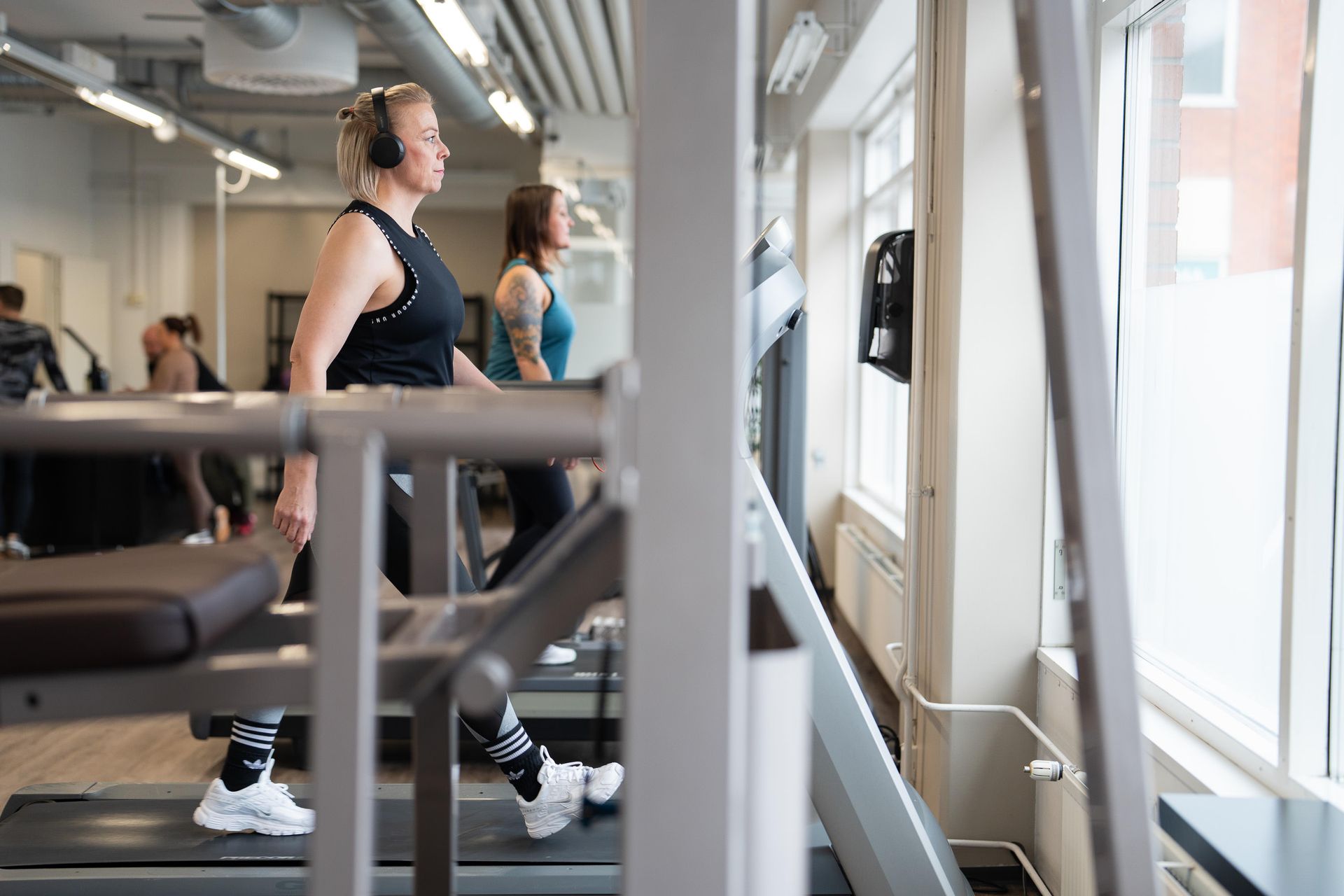 Kuulokkeet päässä oleva nainen juoksee juoksumatolla kuntosalilla.