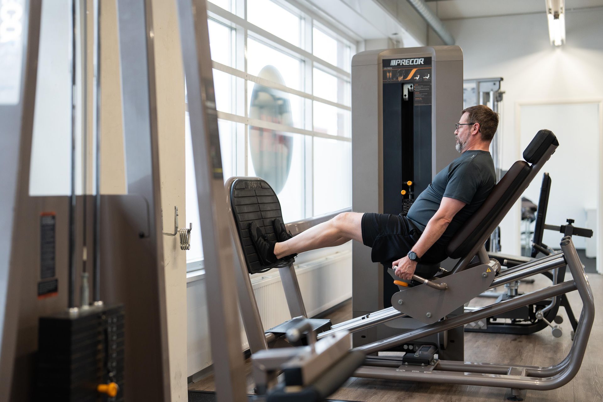Mies käyttää jalkaprässilaitetta kuntosalilla