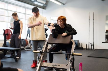 Mies auttaa naista nostamaan painoja kuntosalilla