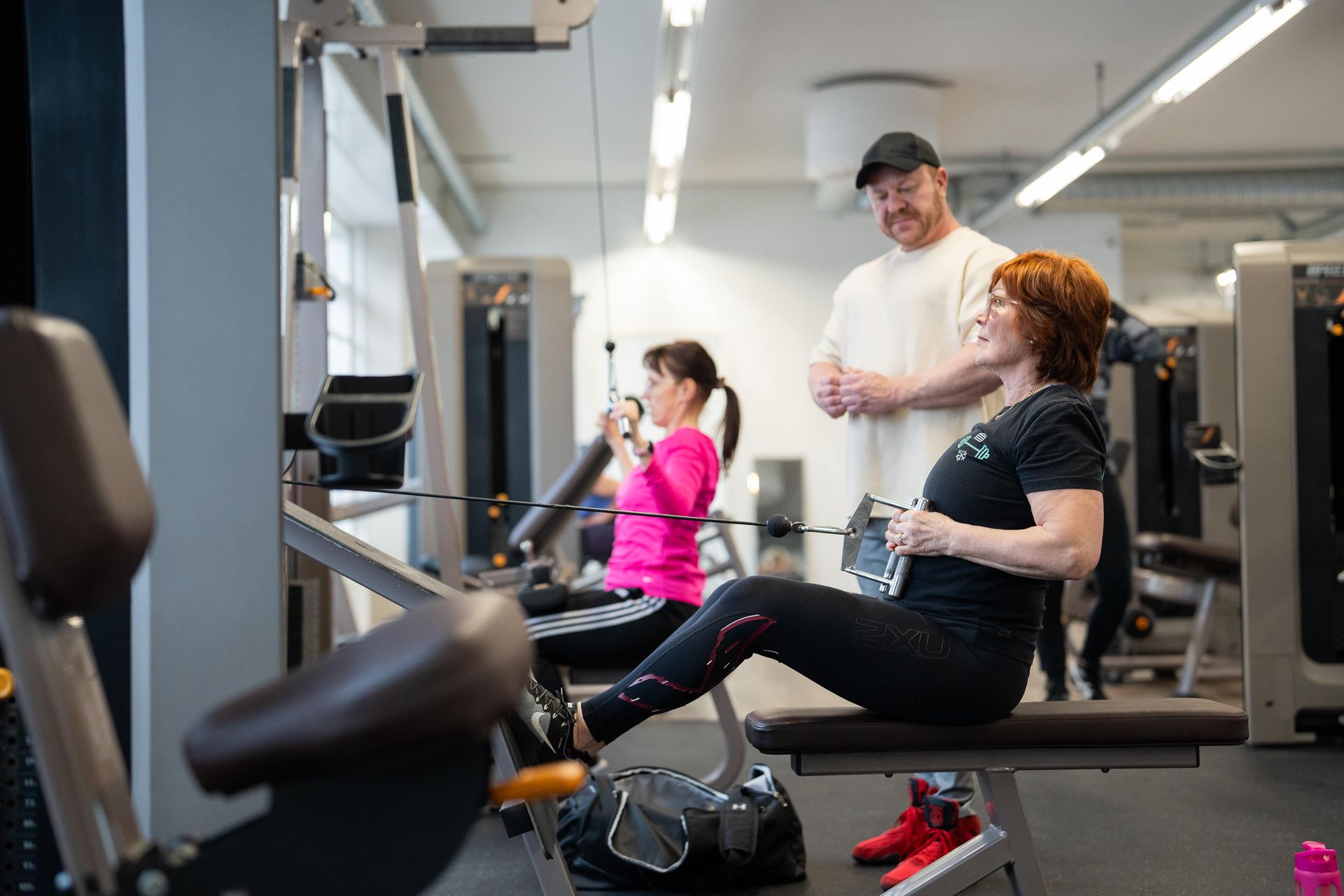 Nainen istuu penkillä kuntosalilla, kun mies puhuu hänelle