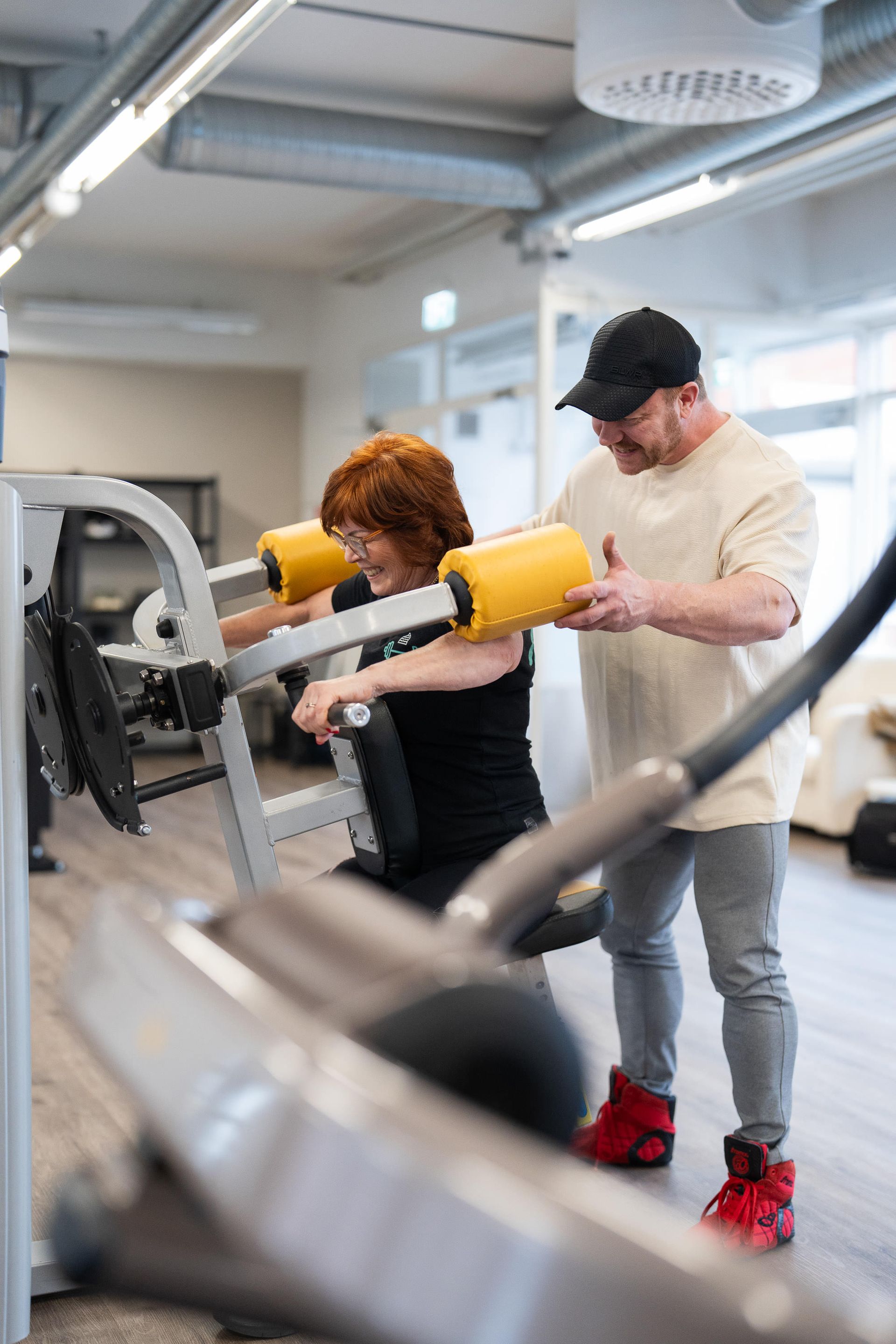 Mies auttaa naista laitteen käytössä kuntosalilla