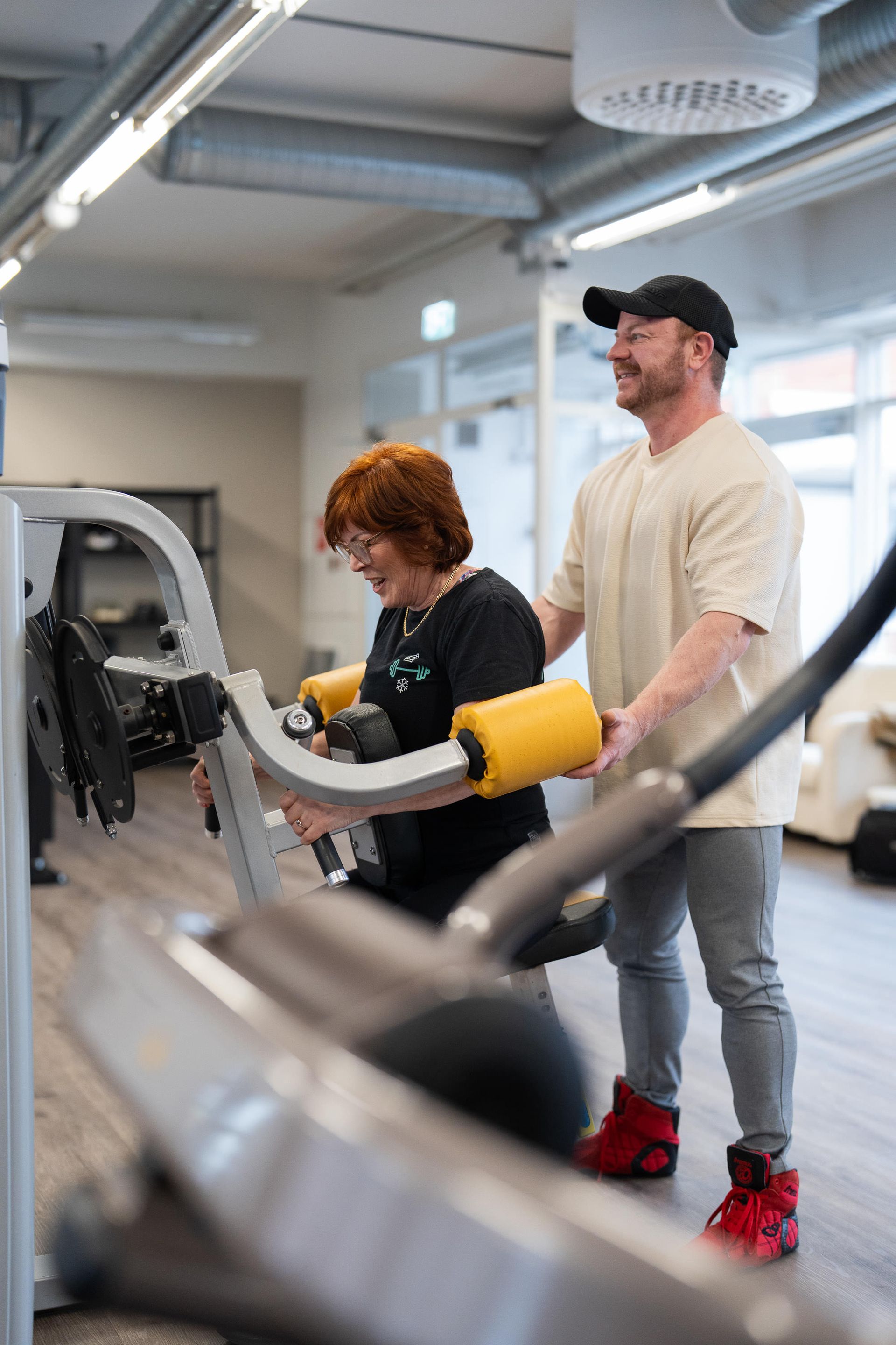 Mies auttaa naista laitteen käytössä kuntosalilla