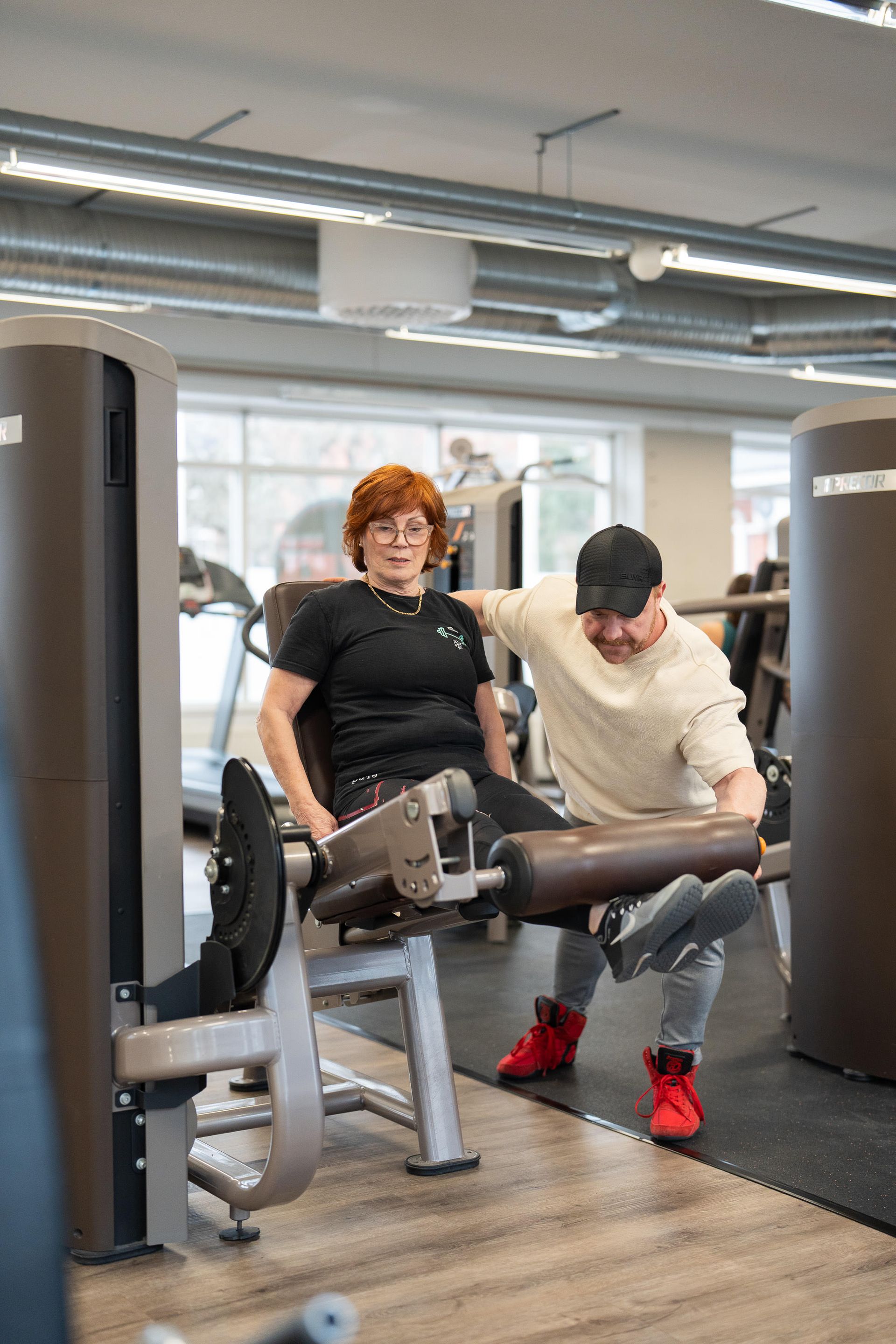 Mies auttaa naista tekemään jalkajumppaa kuntosalilla