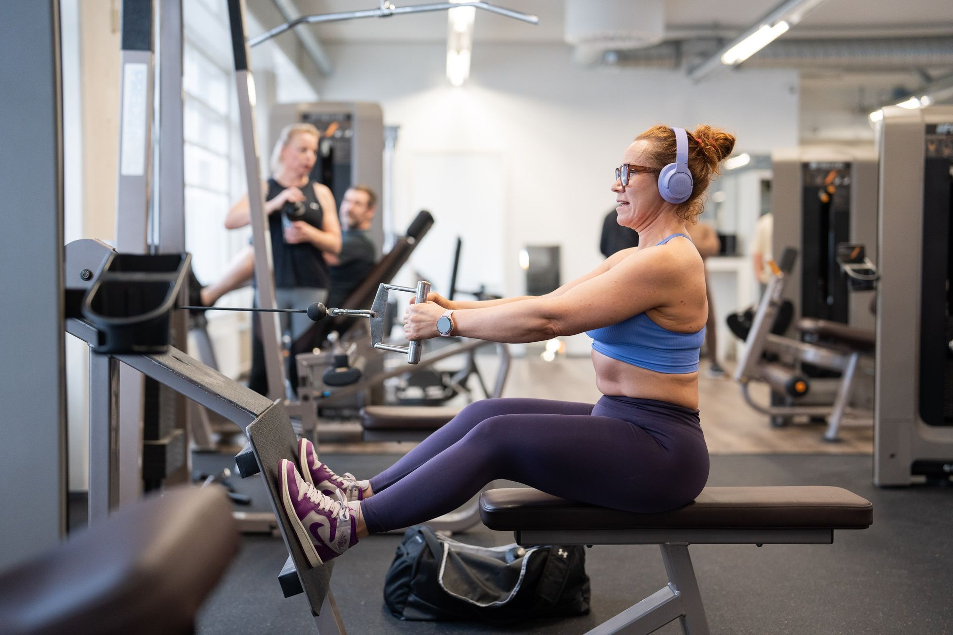 Kuulokkeet päässä oleva nainen istuu penkillä kuntosalilla