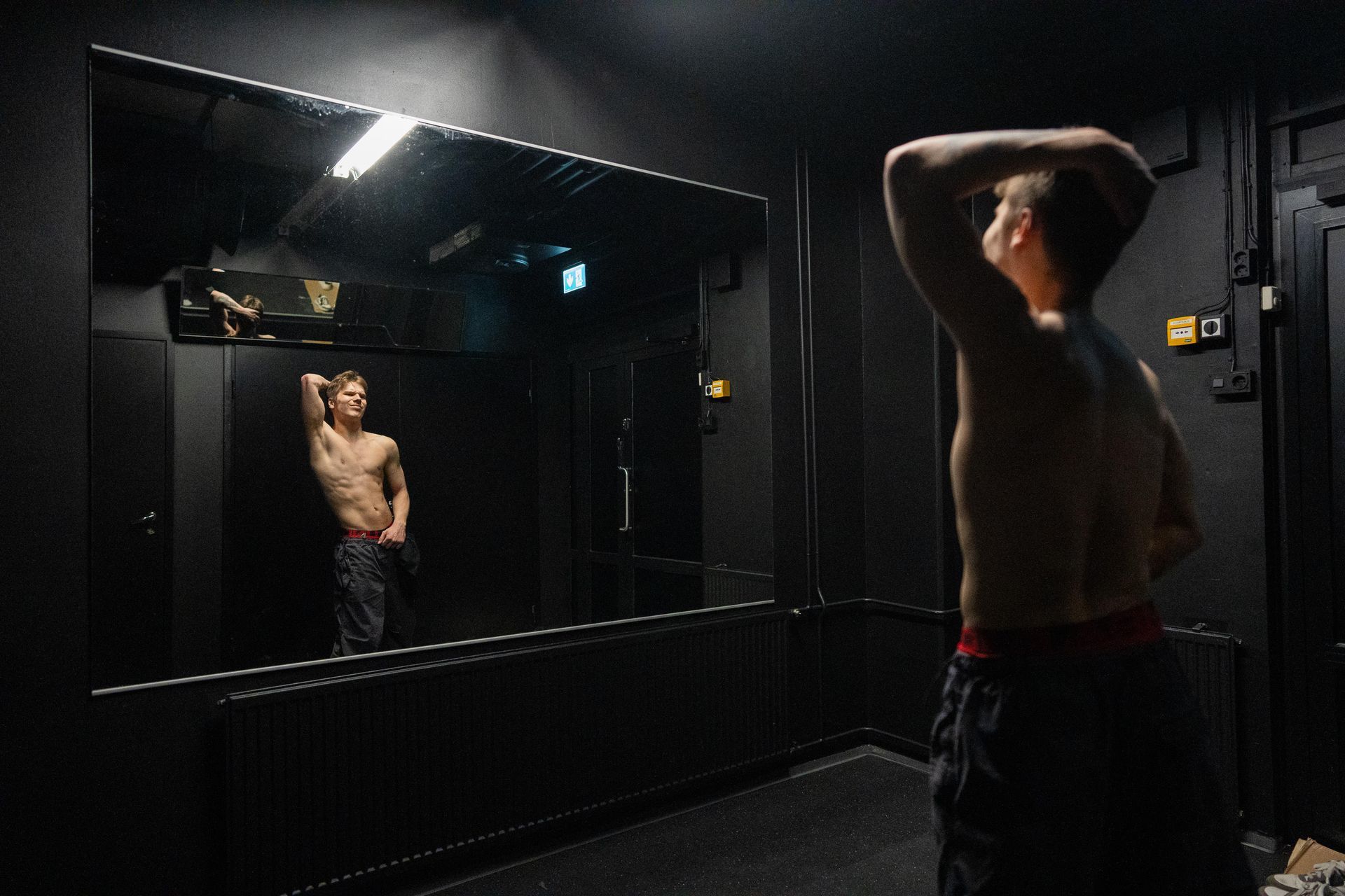 Paidaton mies seisoo peilin edessä pimeässä huoneessa