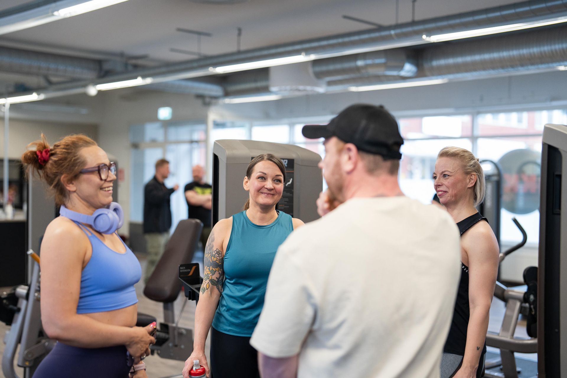 Joukko ihmisiä seisoo kuntosalilla ja keskustelee keskenään