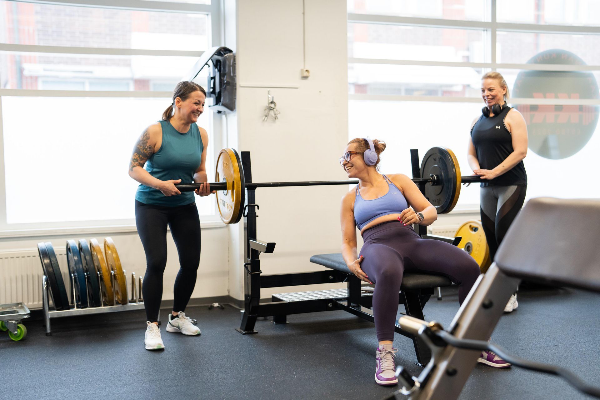 Nainen istuu penkillä kuntosalilla ja puhuu toiselle naiselle