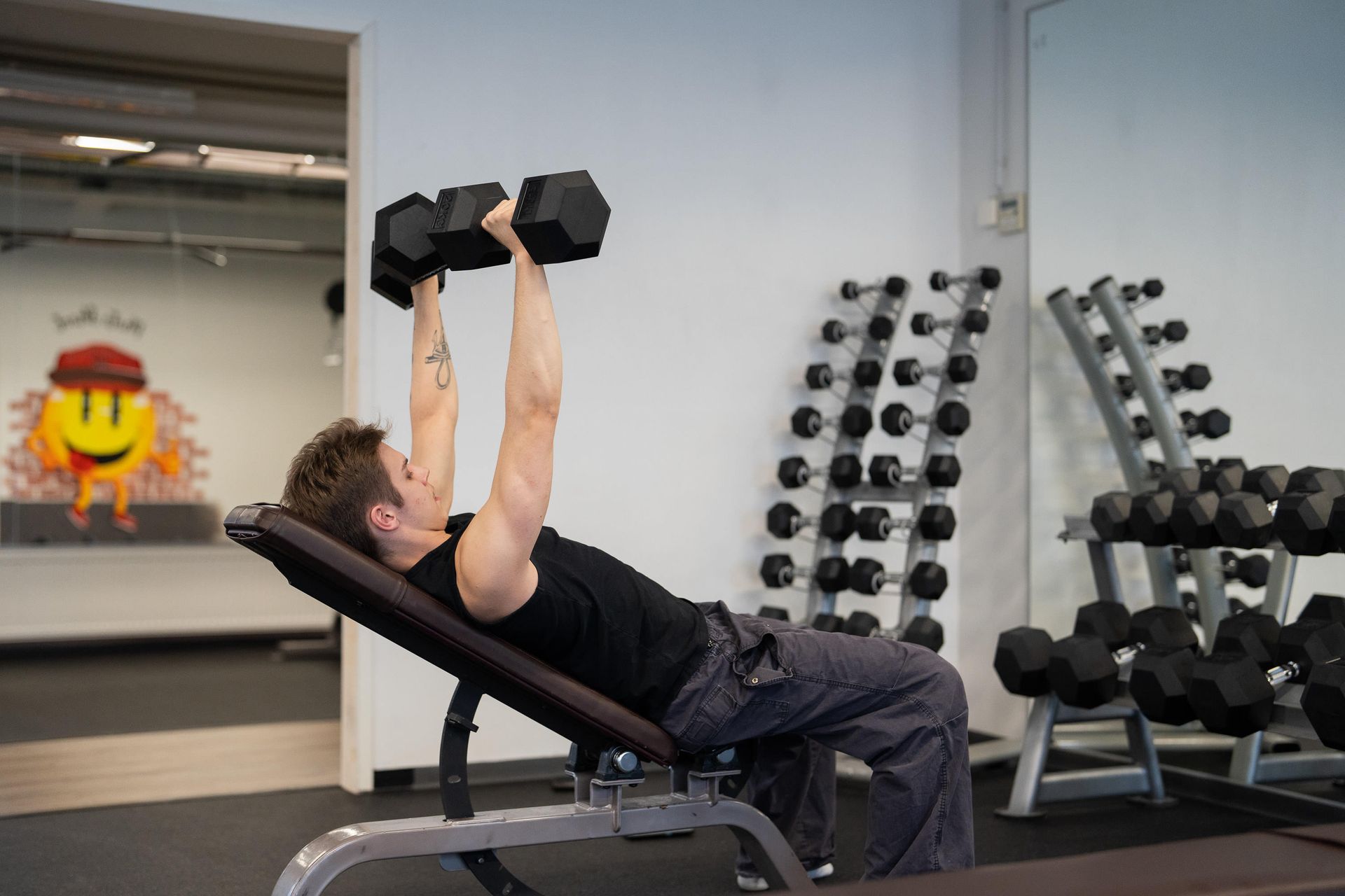 Mies nostelee käsipainoja penkillä kuntosalilla