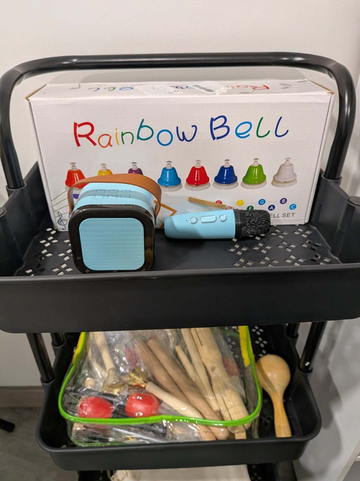 Estantería de juguetes con un juego Rainbow Bell, un micrófono de juguete pequeño y un recipiente con palitos de manualidades y juguetes