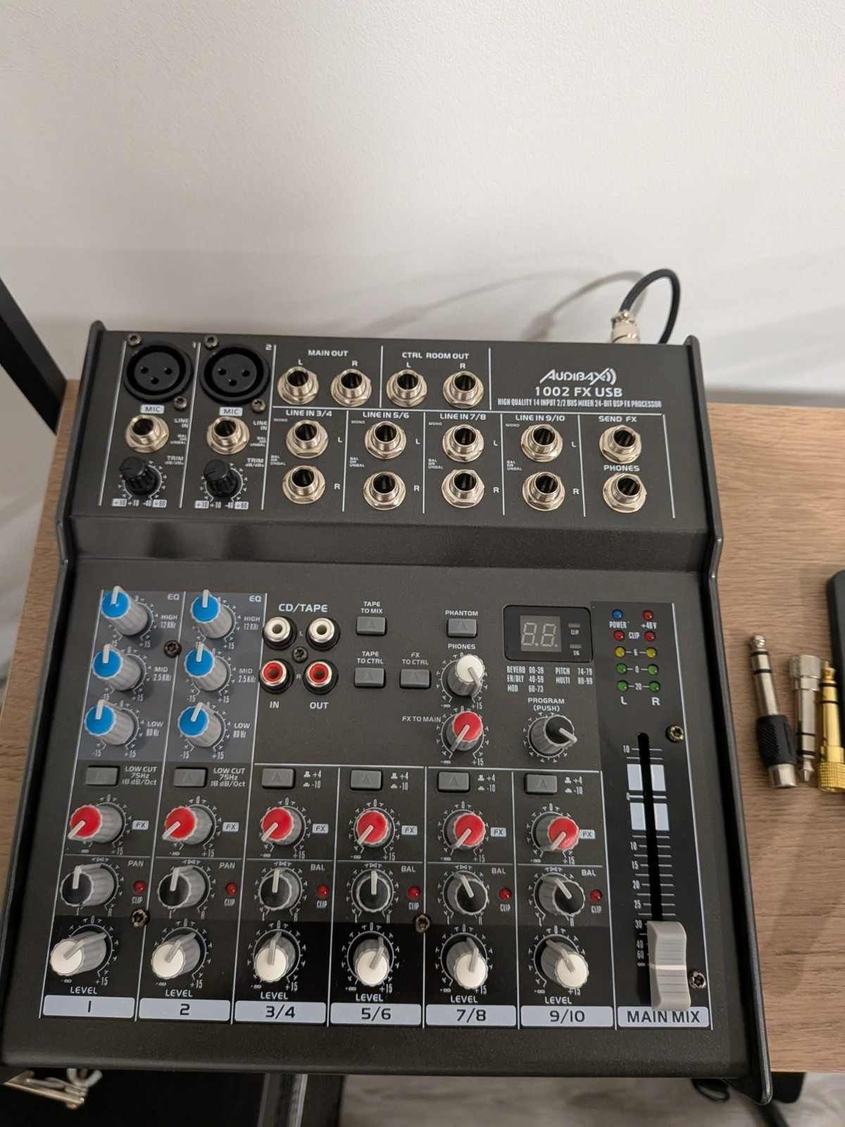 Mesa de mezclas de audio con varios botones, deslizadores y puertos de entrada, junto a varios cables.