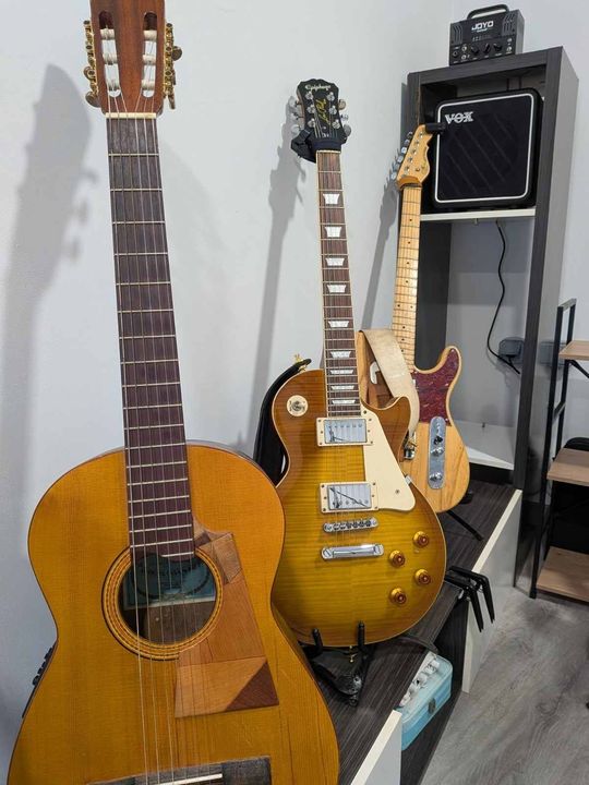 Tres guitarras en soportes junto a un amplificador negro en una habitación.