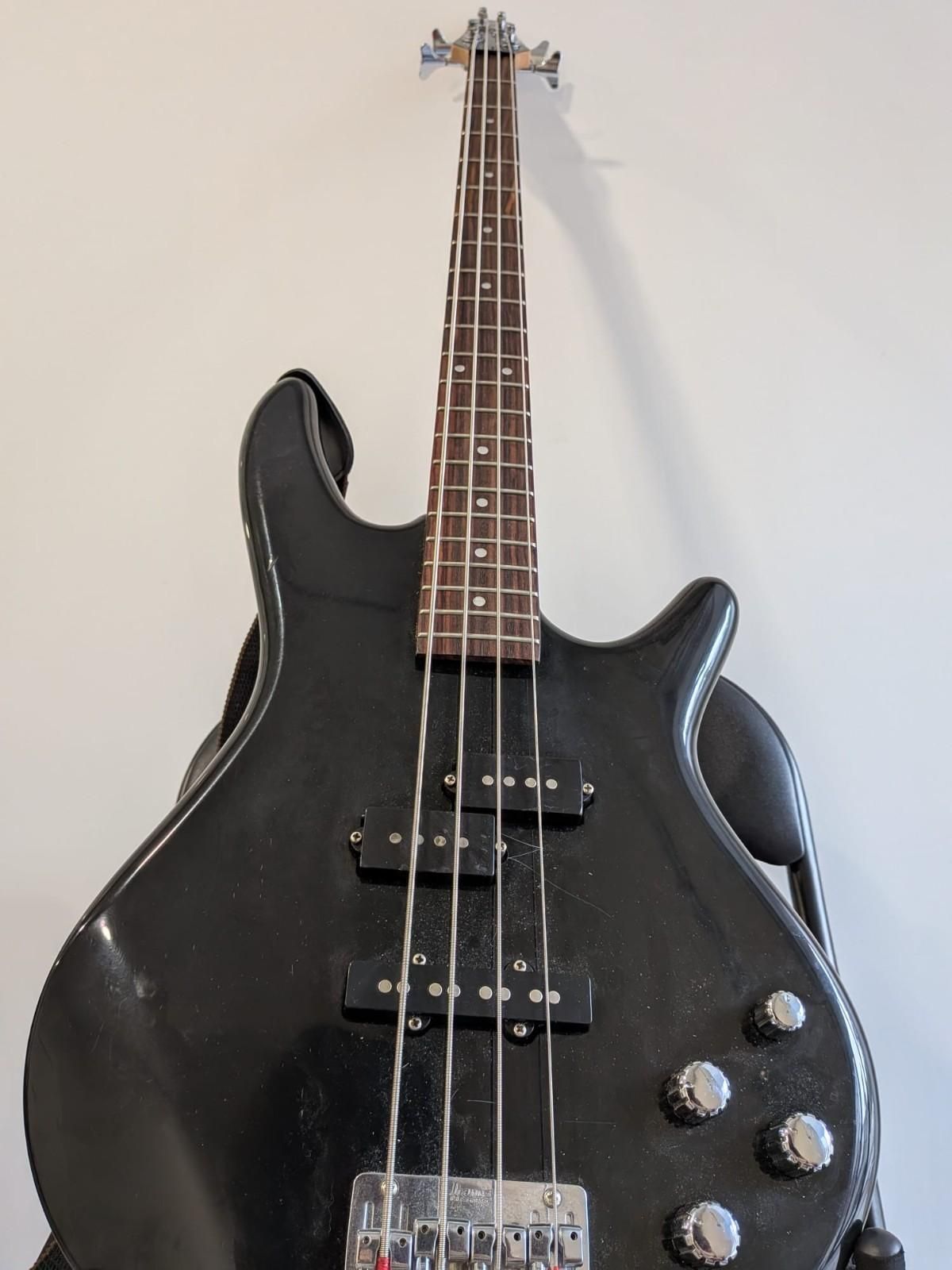 Bajo eléctrico negro con perillas y pastillas cromadas, frente a una pared lisa