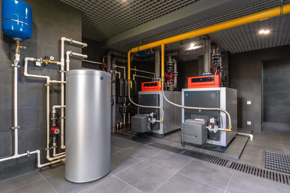 Une chaufferie moderne avec un grand ballon d'eau chaude et deux unités de chauffage industrielles reliées par des tuyaux.
