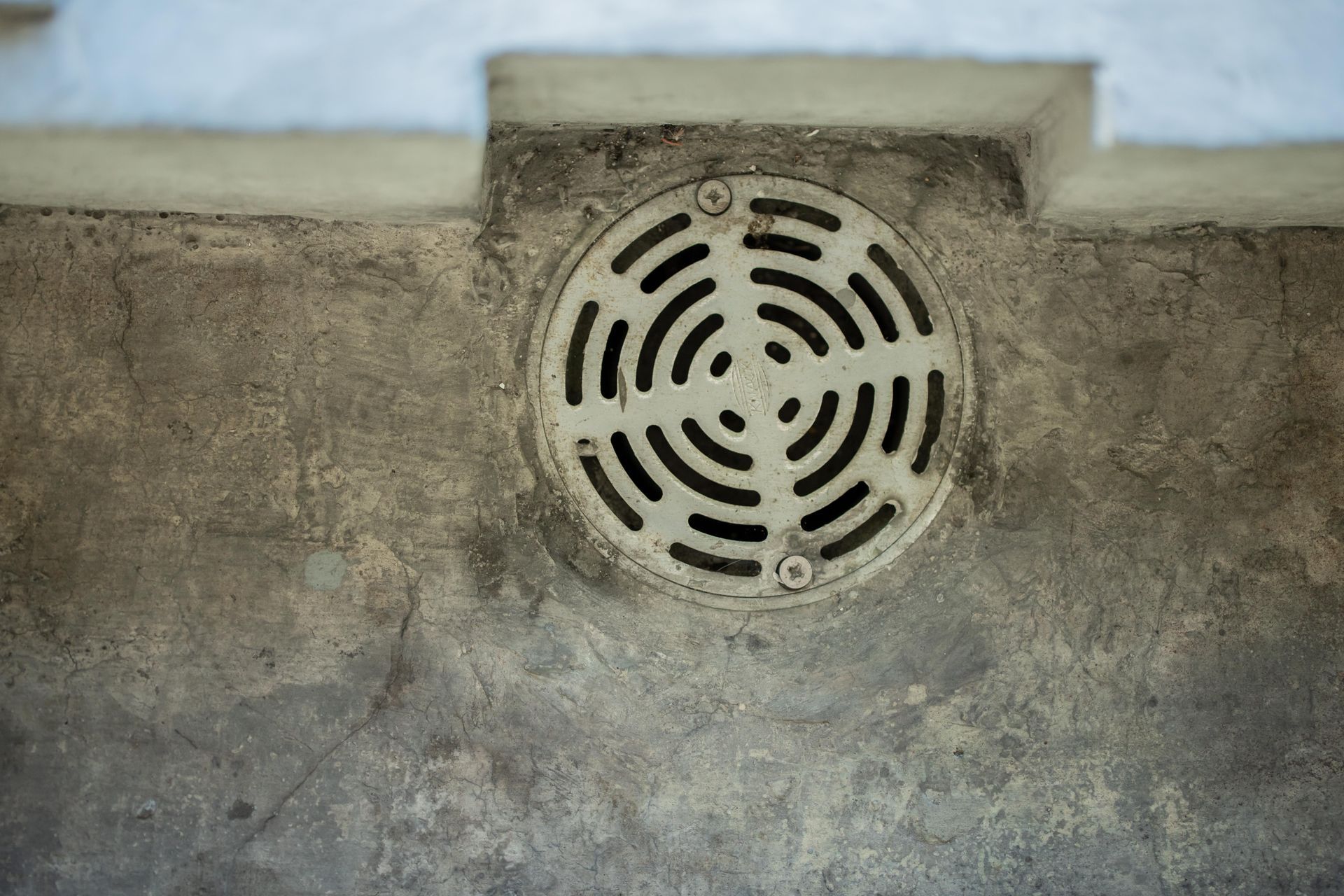 Une grille d'évacuation circulaire en métal encastrée dans un sol en béton.