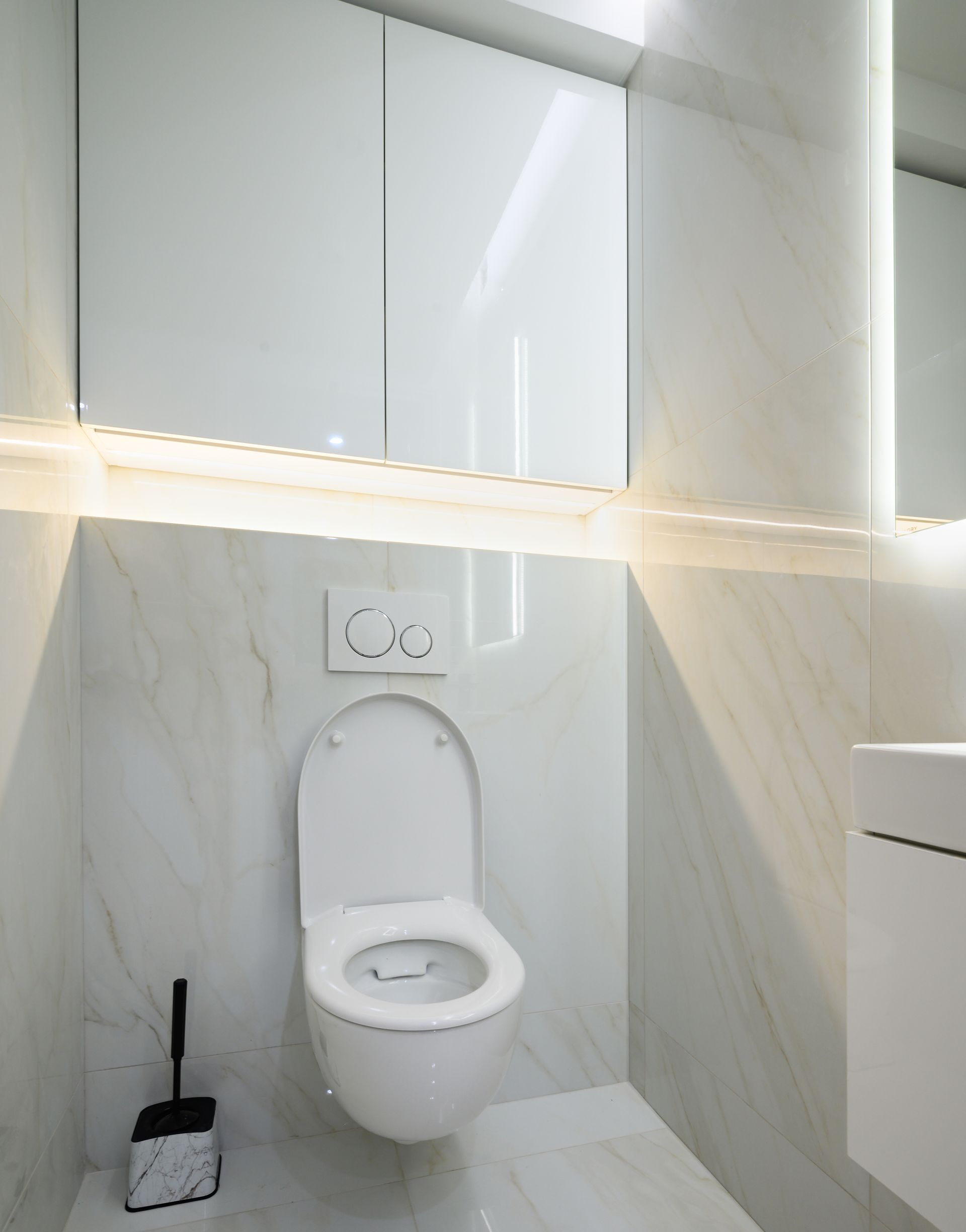 Des toilettes murales modernes dans une petite salle de bains avec carrelage à motif marbre, éclairage sous les meubles et ventouse.