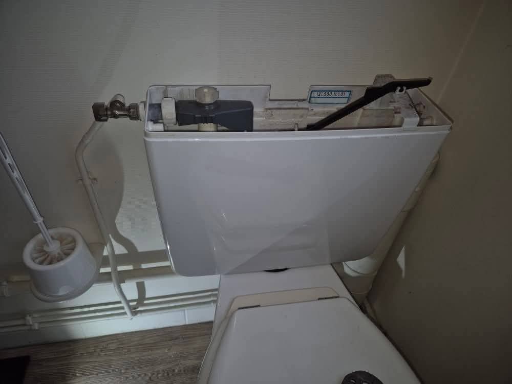 Réservoir de toilettes ouvert, avec mécanismes de chasse d'eau internes visibles.