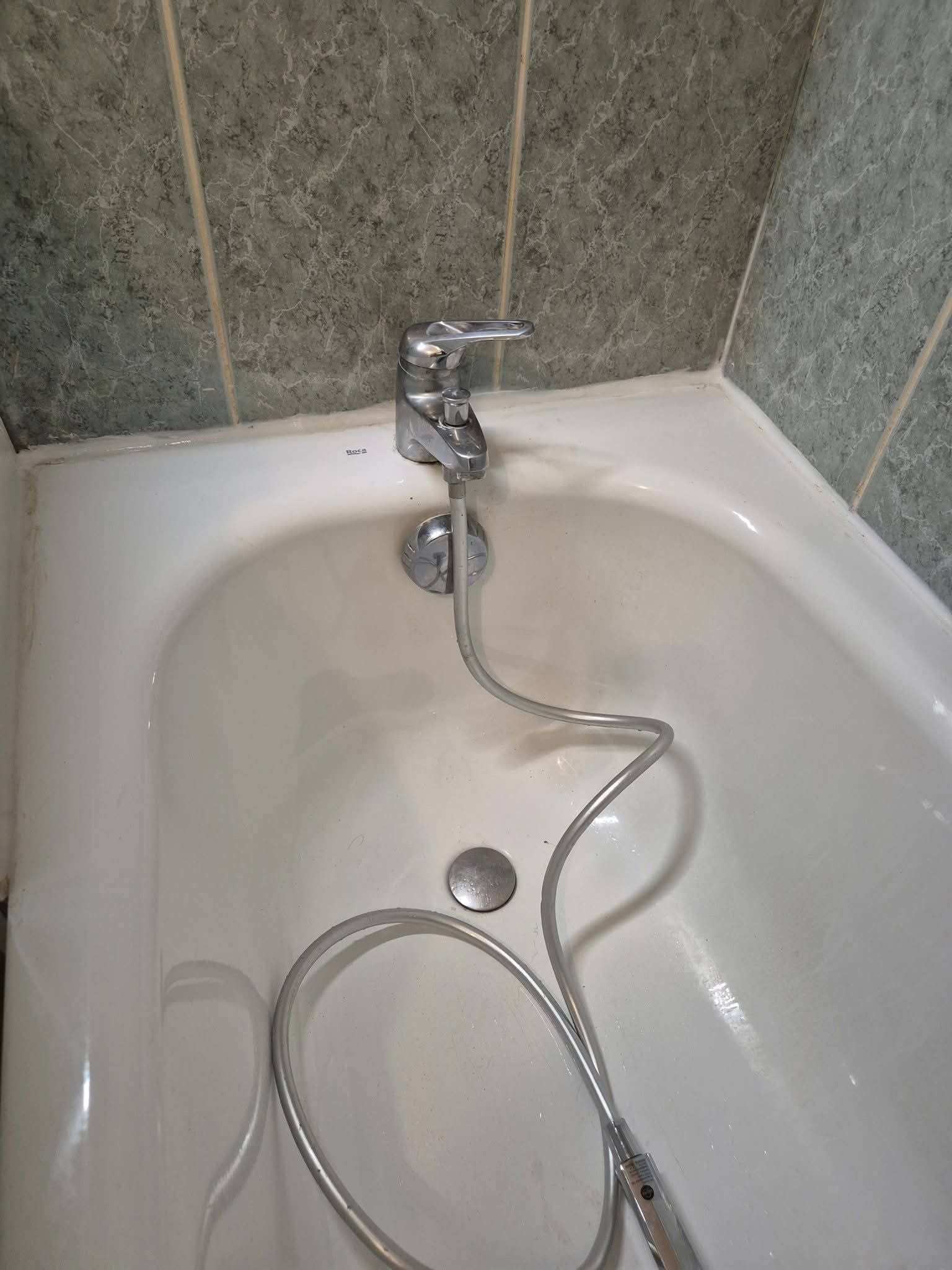 Un robinet de baignoire avec un flexible de douche métallique intégré, le tout sur un fond de mur carrelé.