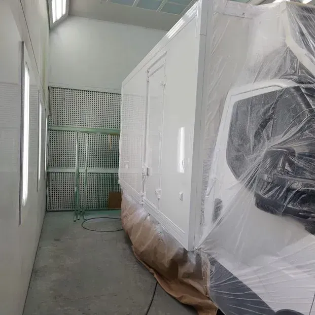 Un camión blanco está cubierto de plástico en una cabina de pintura.
