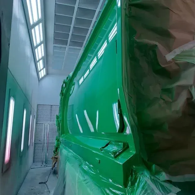 Un camión verde está siendo pintado en una cabina de pintura.
