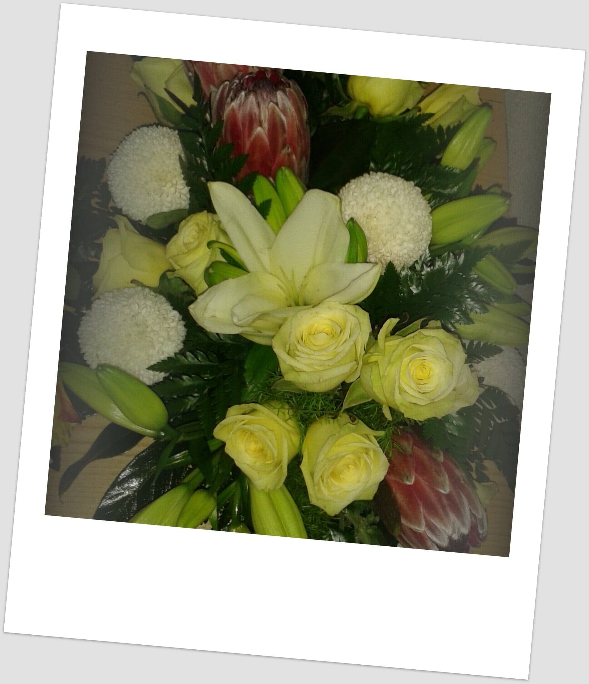 Buquê de flores brancas, amarelas e vermelhas com folhagem verde, em uma moldura estilo Polaroid.