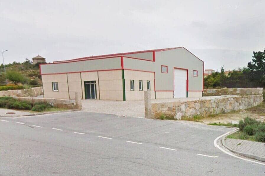 Galpão com paredes cinza-claro, detalhes em vermelho e uma grande porta de garagem branca.